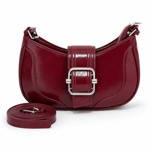 A burgundy crescent-shaped shoulder bag with a glossy patent finish, featuring a central buckle strap closure and a detachable matching shoulder strap placed in front, set against a plain white background.