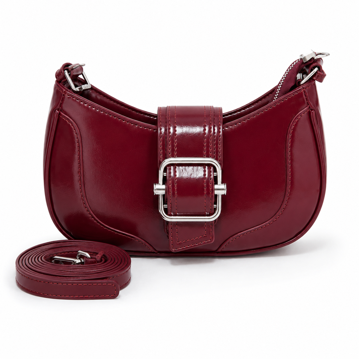 A burgundy crescent-shaped shoulder bag with a glossy patent finish, featuring a central buckle strap closure and a detachable matching shoulder strap placed in front, set against a plain white background.